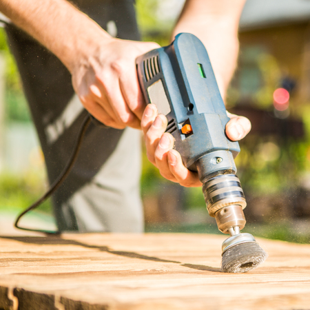 Hands man with electrical rotating brush metal disk sanding a piece of woodの写真素材