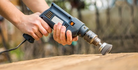 Hands man with electrical rotating brush metal disk sanding a piece of wood