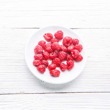 Plate with raspberries on white wooden table.