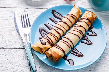 Homemade pancakes or russian blini with chocolate sauce on plate on white wooden background.の写真素材