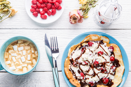 Homemade pancakes or Russian pancakes with chocolate sauce, whipped cream and raspberries on a plate on a white wooden background.の写真素材