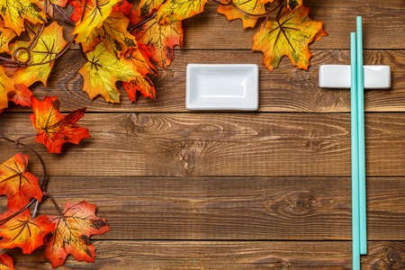 Wooden background with maple leaves, chopsticks for sushi, with place for inscriptionの写真素材