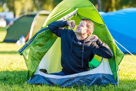 The man woke up, sat down and stretched himself in the tentの写真素材