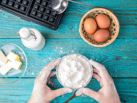 Making waffles at home - waffle iron, batter in bowl and ingredients - milk, eggs and flour.の写真素材