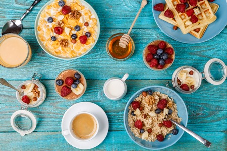 Breakfast table with waffles, oatmeal, cereals, coffee, juice and fresh berriesの写真素材