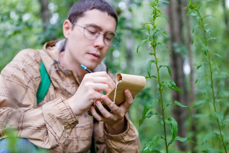 Photo of man writing in notebook among plantsの写真素材