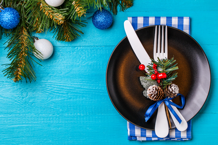 Christmas table place setting with napkin, black plate, white fork and knife, decorated sprig of mistletoe and christmas pine branches.の写真素材