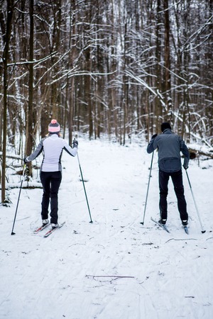 Photo from back of sports woman and man skiing in winter forestの写真素材