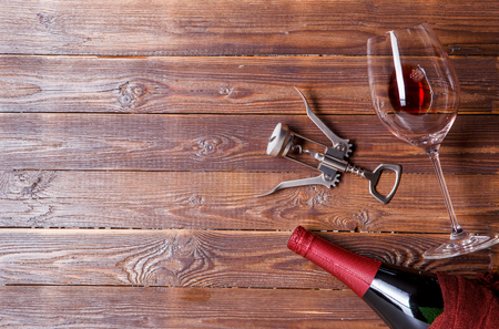 Photo of bottle of wine, corkscrew, wine glass on brown, wooden background.の写真素材