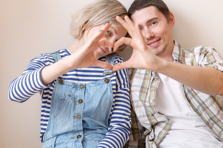 Photo of young married couple with heart from palms sitting on floor among cardboard boxesの写真素材