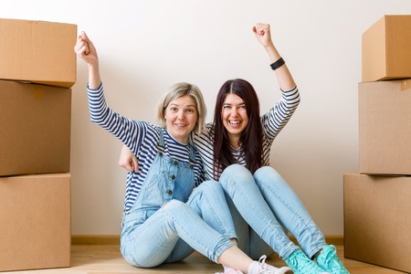 Photo of two girls sitting on floor among cardboard boxes