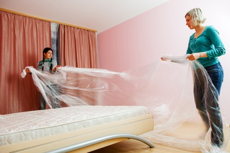 Photo of two young women covering bed with polyethylene