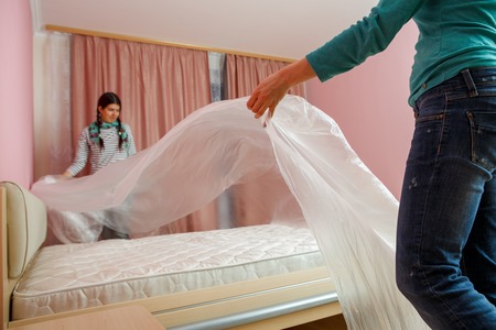 Image of young woman covering bed with polyethylene