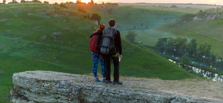 Photo from back of hugging young couple of tourists on mountain