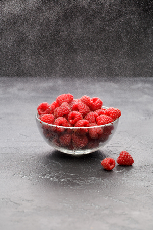 Close-up photo of raspberries in transparent cup on black backgroundの写真素材