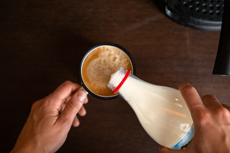 Coffee maker, mans hands pouring milk into mug of coffeeの写真素材