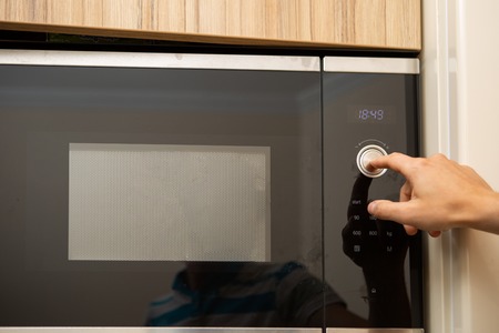 Image of microwave oven and mans hand in kitchenの写真素材