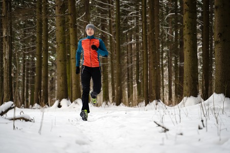 Photo of running athlete among trees in winter forestの写真素材