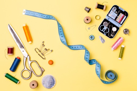 Composition with threads and sewing accessories - scissors, centimeter, pins on yellow background.の写真素材