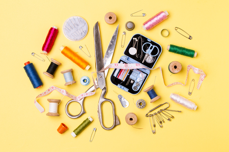 Composition with threads and sewing accessories - scissors, centimeter, pins on yellow background.の写真素材