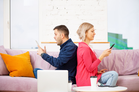 Friends sit on the couch, chatting and using a smartphone, desktop computer.の写真素材