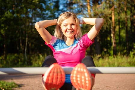 Happy blonde with hands behind head practicing on bench in park on summer.