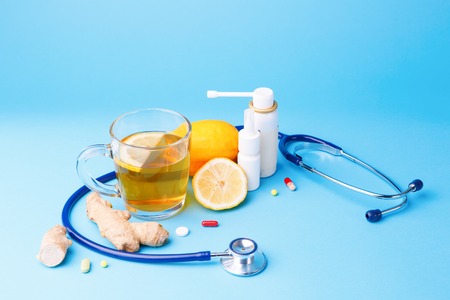 Cold preparations, stethoscope, tea, lemon and ginger root on a blue background.の写真素材