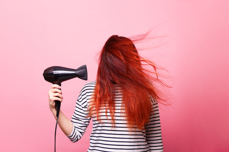 Woman holding a hairdryer on a pink backgroundの写真素材