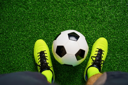 Soccer shoes and football on the green grass