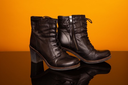 Black half boots with high heel on black glass table and yellow background.