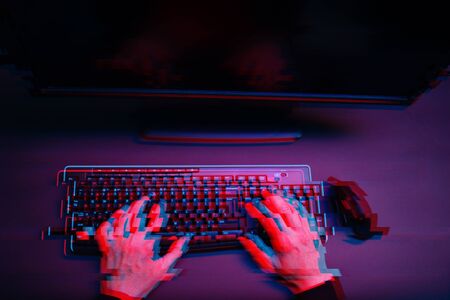 Hacker in the hood working with computer typing text in dark room. Image with glitch effect