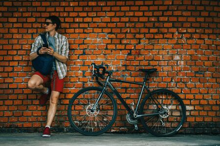 A young stylish man posing next to his bicycle.の写真素材