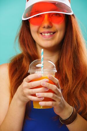 Woman wearing a blue swimsuit, hat and sunglasses drinks fruit juice from a cupの写真素材
