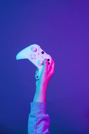 Hand with white gamepad on dark violet background.