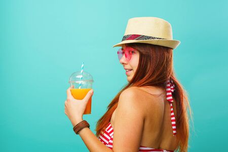 Woman wearing swimsuit and hat drinks fruit juice from a cupの写真素材