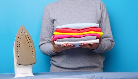 Women with electric iron and pile of clothes in her hands.