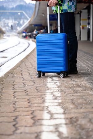 Tourist with blue suitcase at station waiting for train against backdrop of mountainsの写真素材