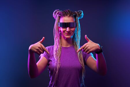 Happy girl with pigtails in sunglasses looking at camera in neon light