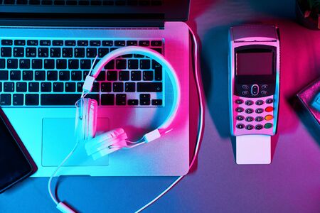 Laptop with headphones, phone, gift box and pin pad with payment card in neon colors. Concept of internet shoppingの写真素材