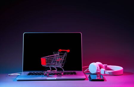 Laptop with headphones, phone and customer trolley on the table in modern neon colors.の写真素材