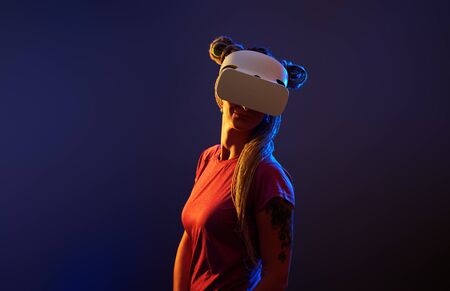 Woman is using virtual reality headset. Neon light studio portrait. Concept of virtual reality, simulation, gaming and future technology.の写真素材