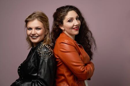 Blonde and brunette women in leather jacket looking at camera isolated in studio