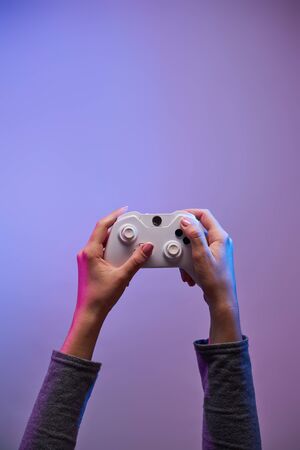 Female hands with a game joystick on violet background. Gamer concept.の写真素材