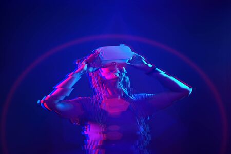 Woman is using virtual reality headset. Neon light studio portrait. Concept of virtual reality,...