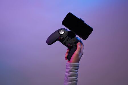 Female hands with a game joystick with smartphone on violet background.の写真素材