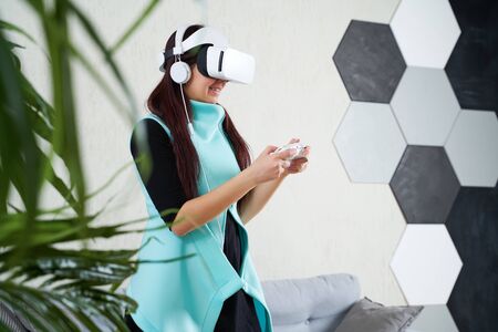Woman with virtual reality headset and gamepad is playing game.