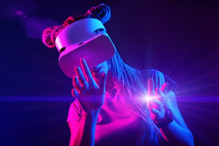 Woman is using virtual reality headset. Neon light studio portrait. Concept of virtual reality, simulation, gaming and future technology.の写真素材