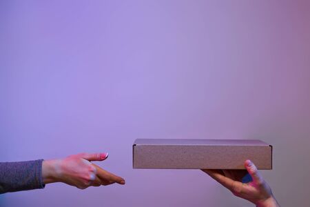 Two hands with cardboard box on blank purple background.