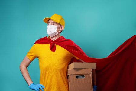Courier with boxes is wearing urgical face mask in superhero cloak.の写真素材