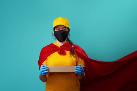 Courier with box is wearing in superhero cloak and protected face mask.の写真素材